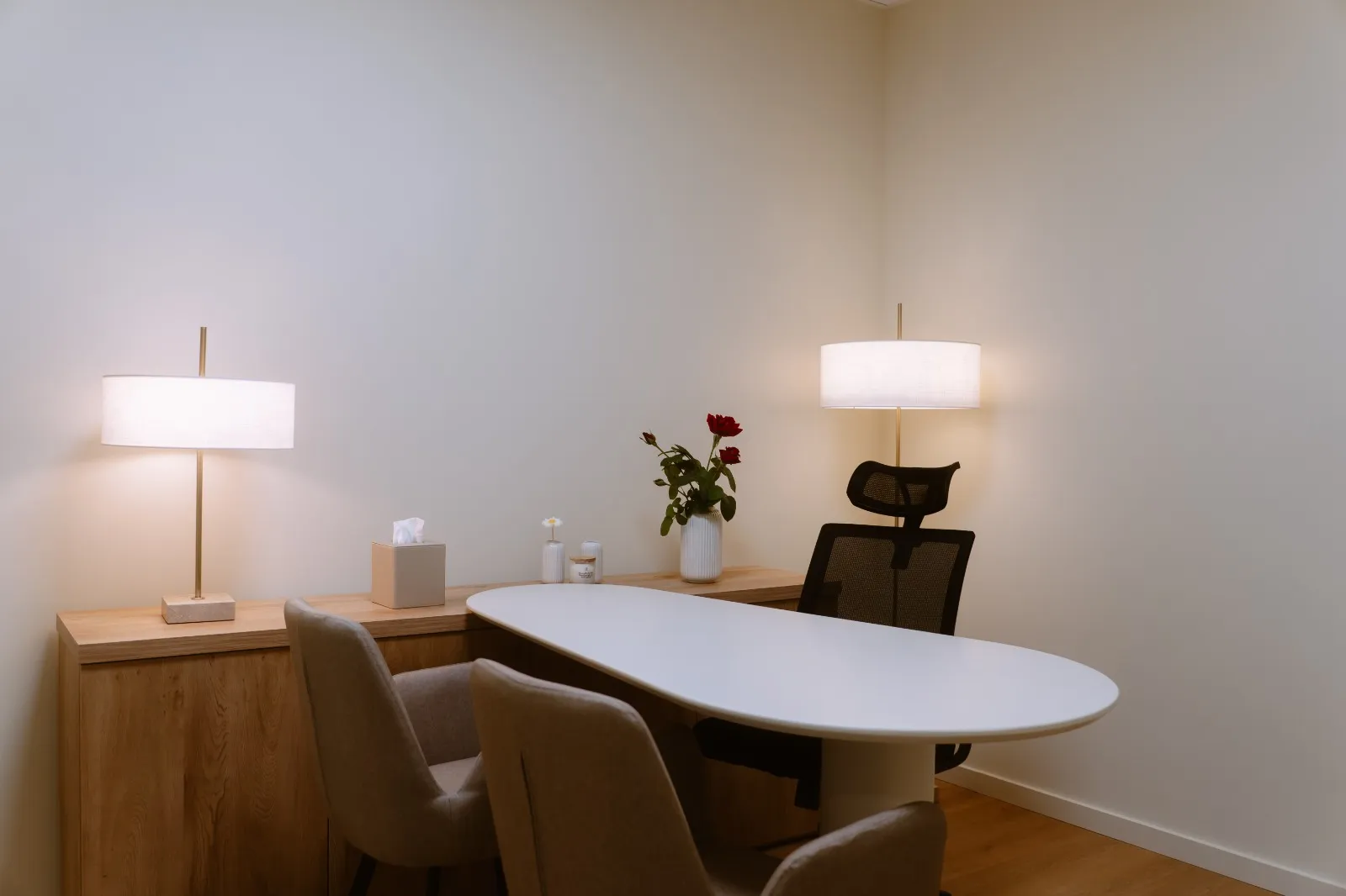 Sala de consulta com mesa branca, candeeiro e flores