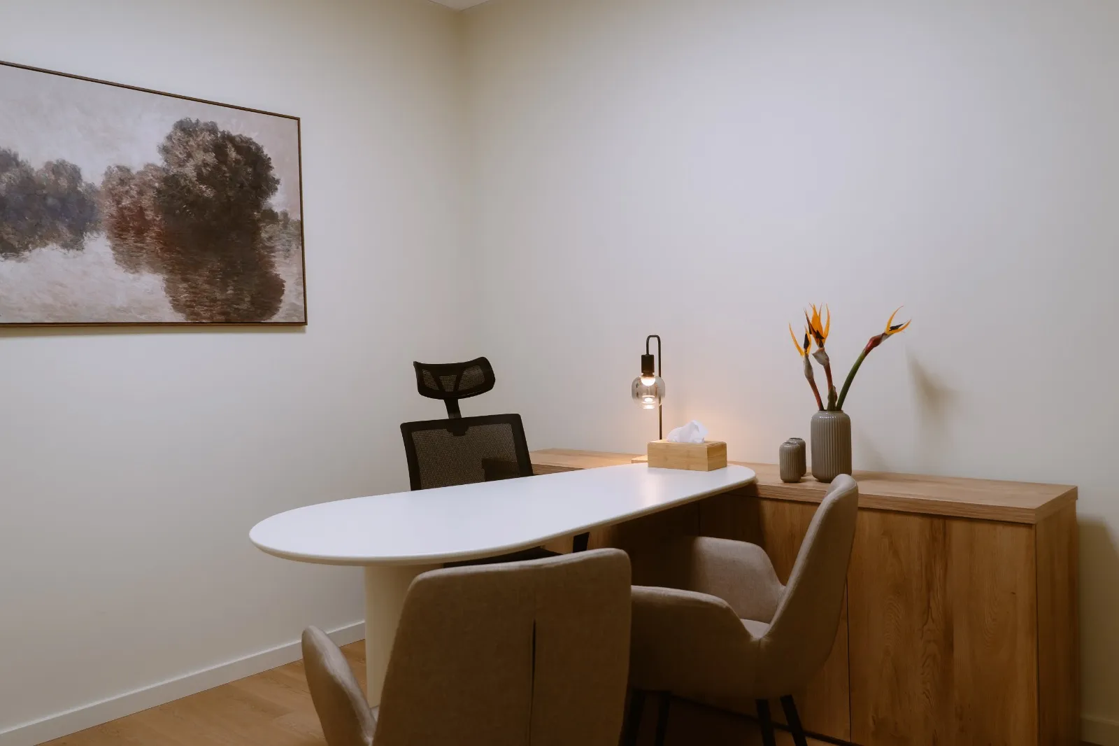 Sala de consulta com duas cadeiras estofadas, mesa branca e quadro na parede